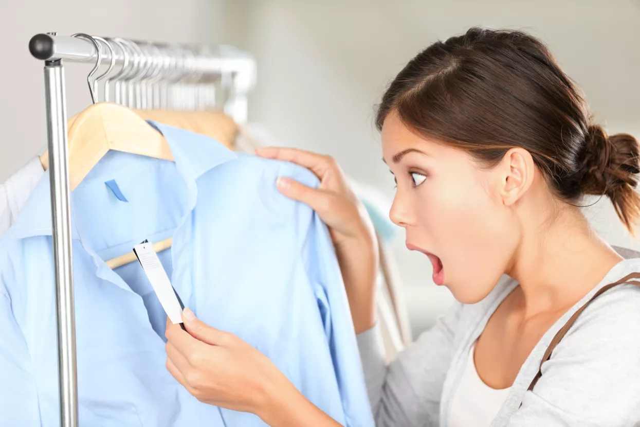 Shopping woman shocked over price tag. Funny shopper woman staring amazed at price. Mixed race Caucasian/Asian Chinese young female model in clothing shop.
