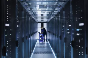 IT Engineer With Crash Cart Puts Hard Drives into Open Rack Server Cabinet. He's Working in Big Data Center.
