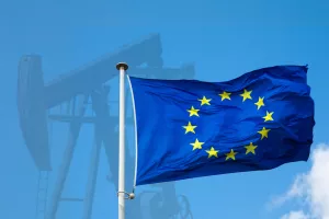 EU flag close-up against the background of an oil pump and a blue sky on a clear day. The concept of oil supplies to Europe.Europa, EU, industrijska proizvodnja, industrija