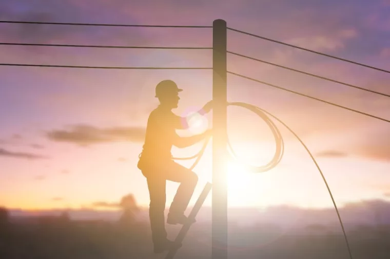 Silhouette of a utility worker climbing a pole and handling fiber optic cables during sunset. Concept of communication technology, internet installation, and telecommunication service. copy spaceoptika, optički internet, internetska infrastruktura, mreža, telekomi, gradnja mreže