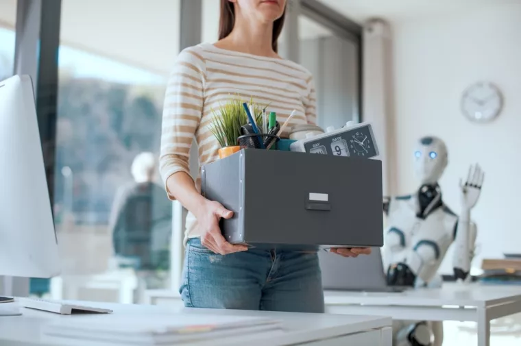 Fired office worker leaving her workplace and humanoid robot staring at herthe impact of AI on employment, silent firing, quiet firing, umjetna inteligencija, radno mjesto, otkaz, otkazi, otpu&scaron;tanje, AI